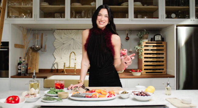Dua Lipa cooks in a modern kitchen with fresh ingredients on the kitchen counter