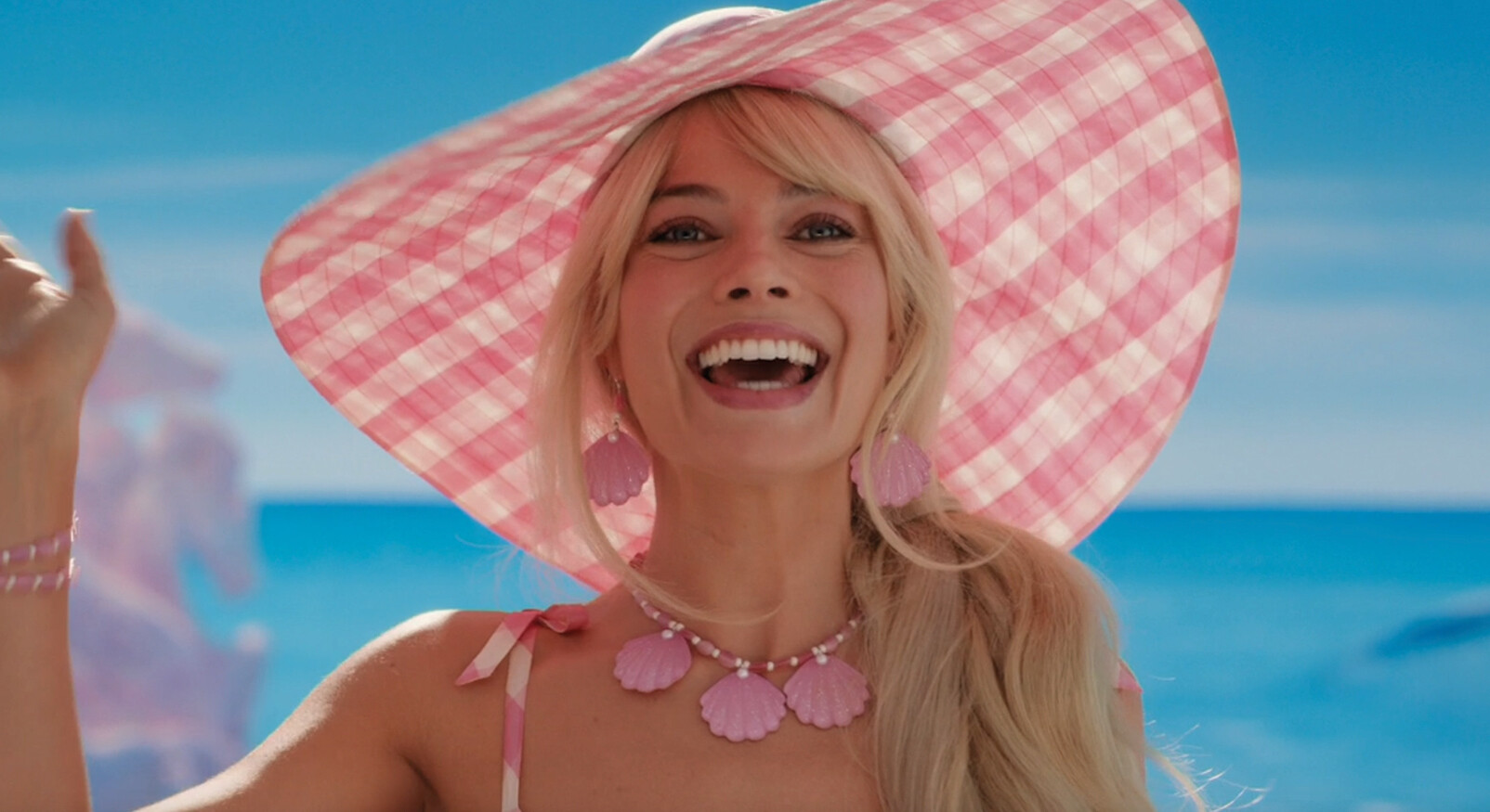 Blonde vrouw barbie margot robbie lachend op het strand met roze hoed