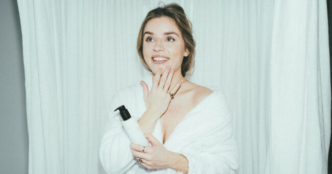 Lotte van scherpenzeel in een witte badjass bij de douche met douche gel in haar handen