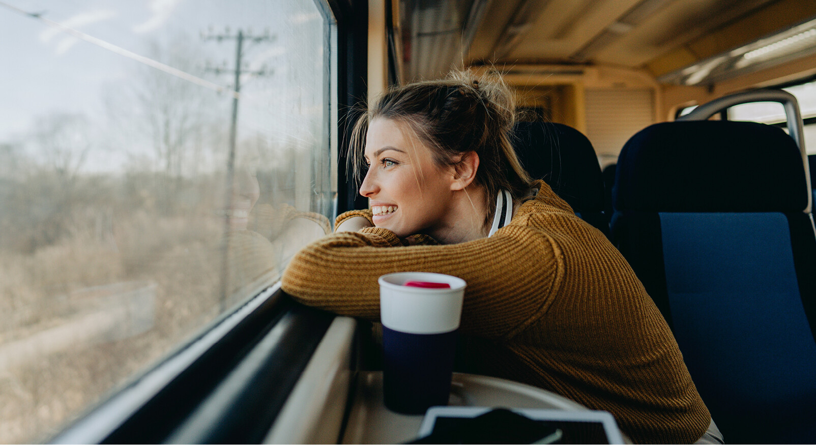 vrouw kijkt lachend naar buiten in de trein met koffie