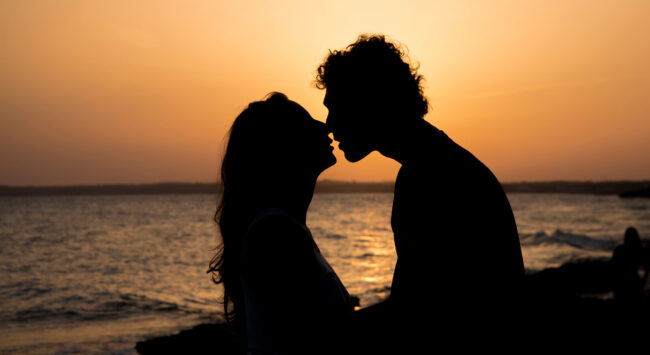 man and woman kissing with sunset in the background
