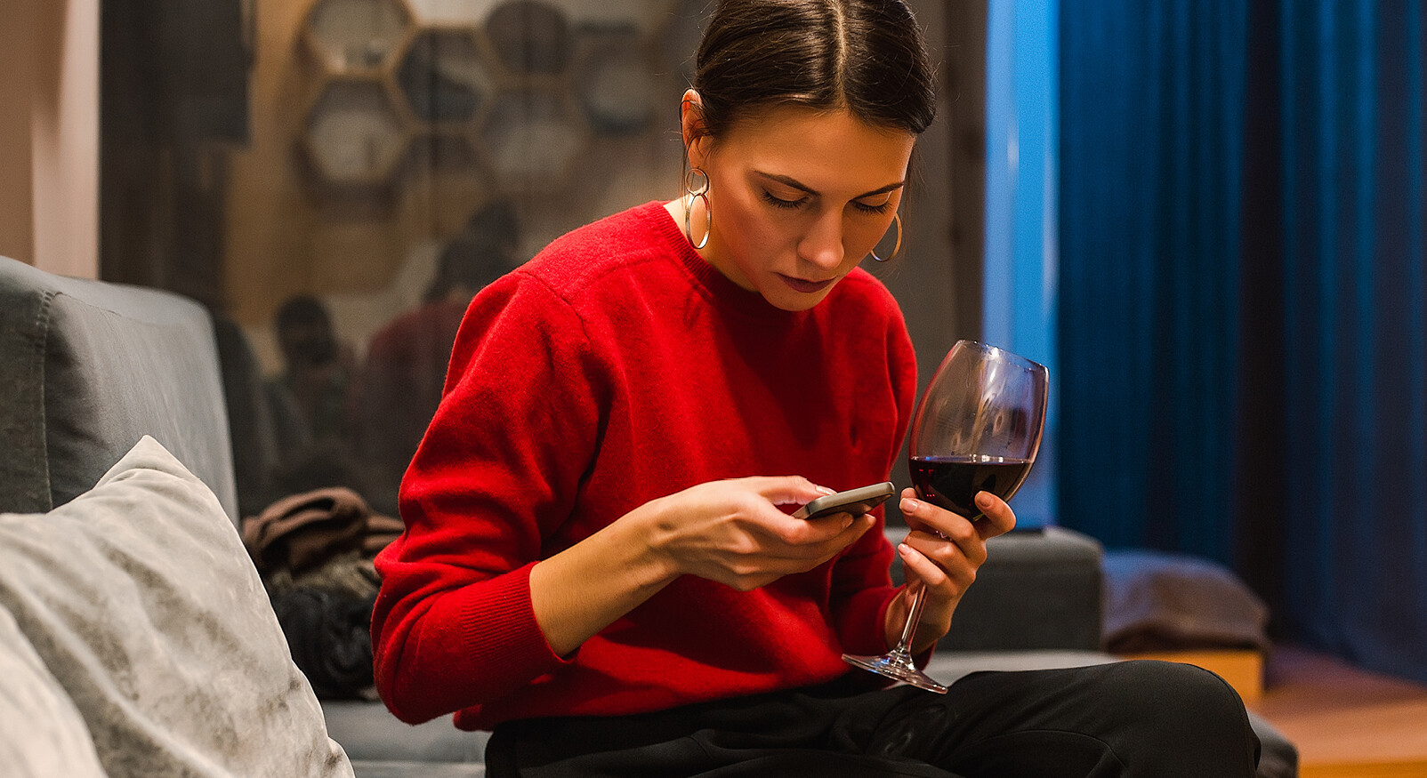 vrouw achter telefoon kijkend met een glans wijn