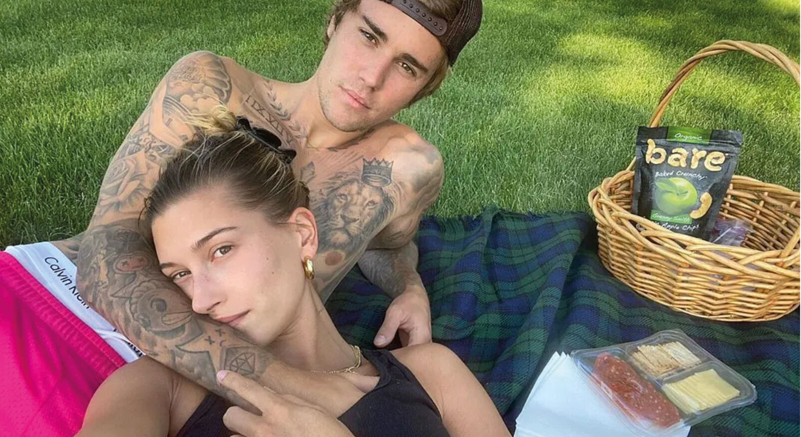 justin en hailey bieber op de grond in het gras aan het picknicken in de natuur met mandje eten chips en vleeswaren