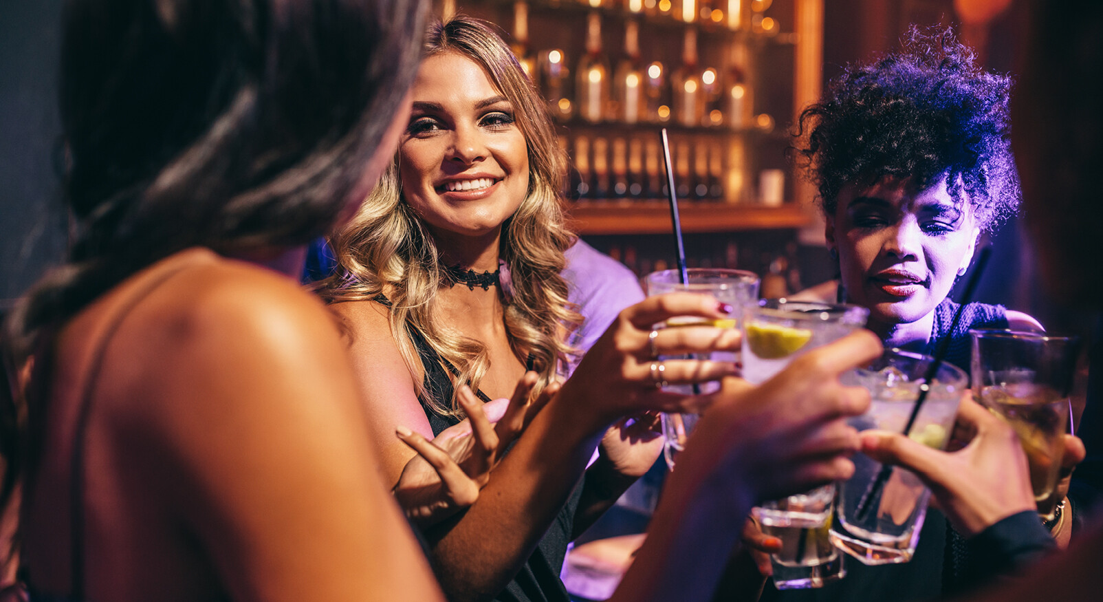 vrouwen proosten bij uitgaan in een club lachend blond en krullend haar cocktails feesten lachend