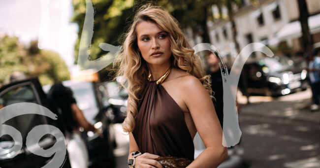 woman with long blonde hair looking seriously ahead with zodiac signs around her on the street