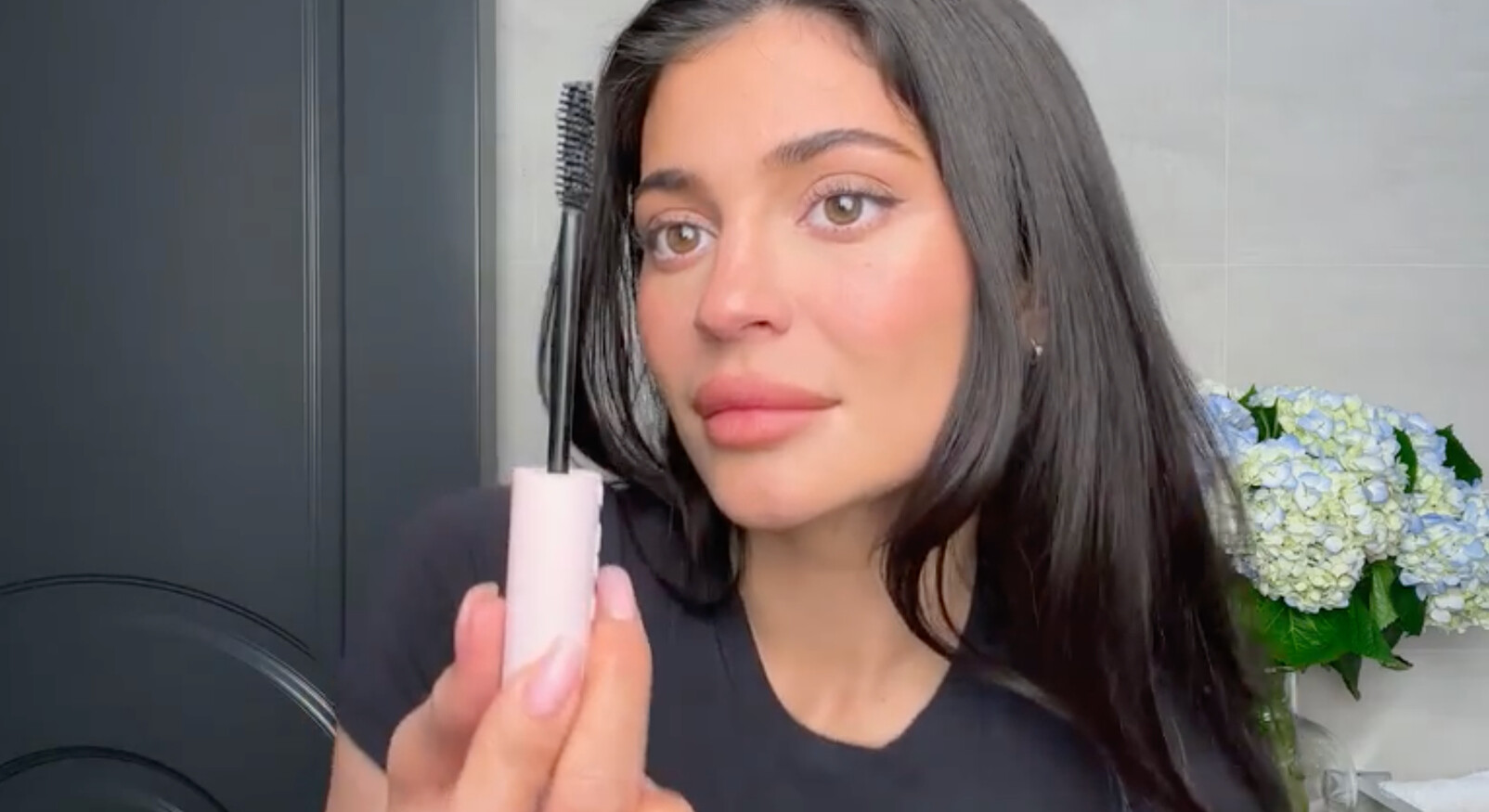 kylie jenner in een make-up video mascara op haar wimpers aanbrengen zwarte top badkamer bloemen op de achtergrond