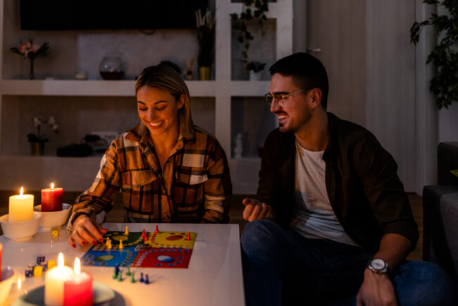 A young couple is sitting at home and playing a board game in the dark during an energetic crisis.