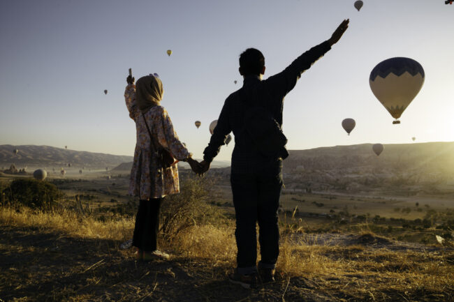 young muslim couple enjoy the sunrise with view of hot balloon in goreme