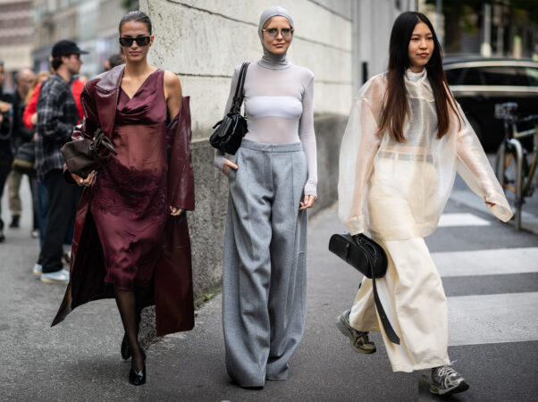 Een collage van drie vrouwen met diverse mode-items. Links draagt een vrouw een donkergroene jas over een witte kanten tuniek met een lichtblauwe spijkerbroek. In het midden draagt een vrouw een zwarte satijnen top met kant en een lange leren jas over een oversized spijkerbroek. Rechts draagt een vrouw een donkere trenchcoat over een witte kanten blouse en een geruite midi-rok, met een gestippelde hoed
