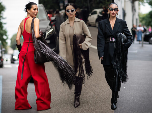 Een collage van drie vrouwen in grijze pakken en overhemden met stropdassen. Links draagt een vrouw een oversized grijs colbert en een grijze pantalon met zwarte accessoires. In het midden draagt een vrouw een grijze blazer over een wit overhemd met stropdas, een geruite blouse om haar middel geknoopt en een grijze pantalon. Rechts draagt een vrouw een wit overhemd met een stropdas, een oversized grijze pantalon en een geruite wollen baret.