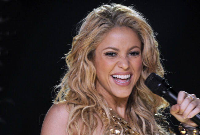 Zangeres Shakira lacht en zingt in een gouden top tijdens een live optreden, gelinkt aan Lewis Hamilton in 2023.