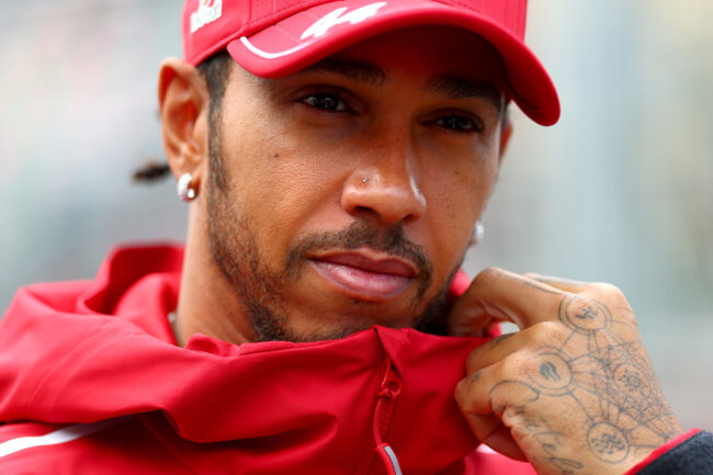 Lewis Hamilton met rode pet en neuspiercing poseert op het circuit, gefocust op zijn werk.