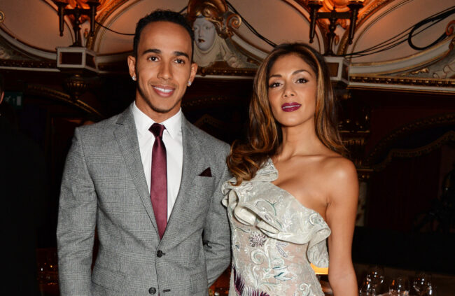 Lewis Hamilton in een grijs geruit pak naast zangeres Nicole Scherzinger in een galajurk