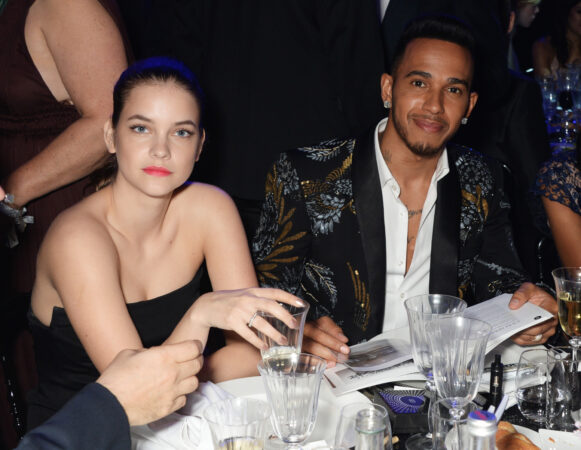 Model Barbara Palvin en Lewis Hamilton in een feestelijke geborduurde smoking zitten aan een gala tafel in 2016.