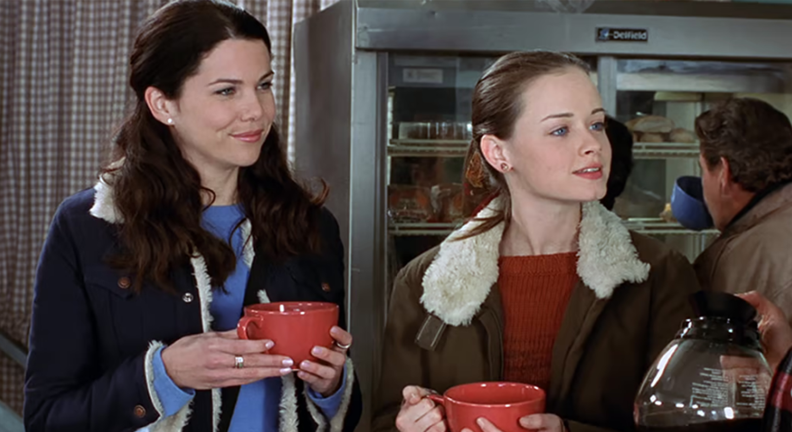 Lorelai en Rory Gilmore in hun typische herfstkleding met warme dranken in een diner, wat een gezellige herfstvakantie-sfeer oproept.
