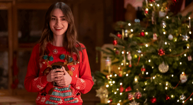 Vrouw in een rode kersttrui lacht voor een verlichte kerstboom, met een warme drank in haar handen.