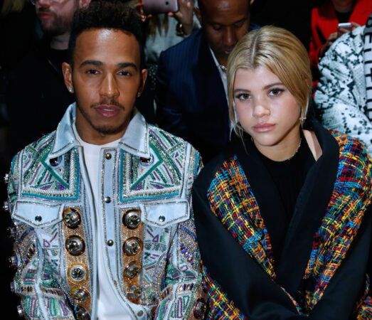 Lewis Hamilton in opvallend bewerkt spijkerjack naast Sofia Richie in een kleurrijke mantel op de Parijs Fashion Week 2017.
