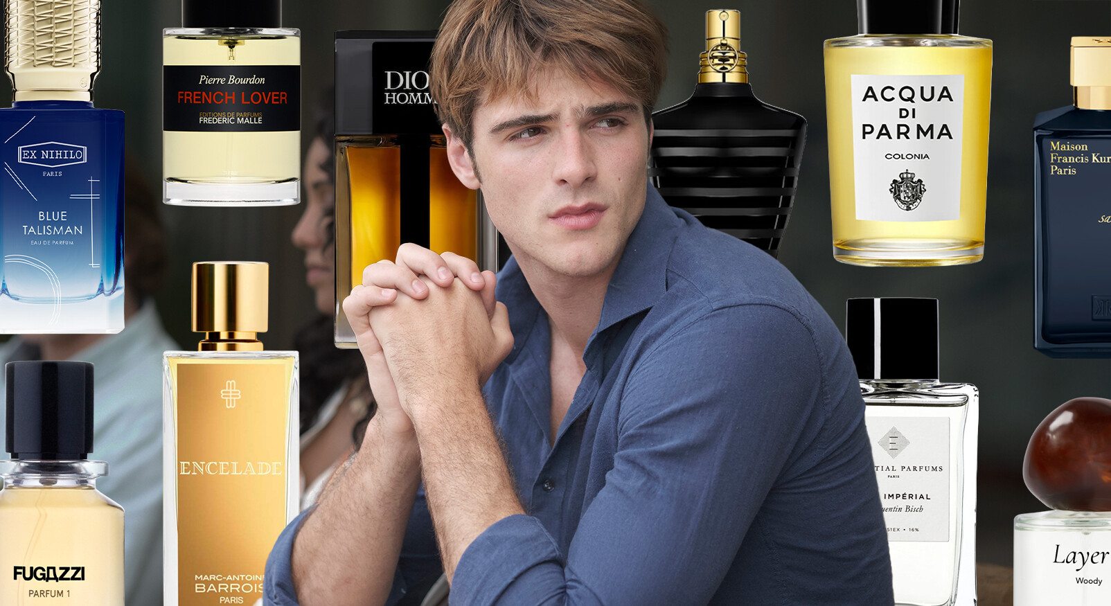 "A young man with brown hair and a blue shirt looks to the right with his hands folded in front of his face. He is surrounded by various bottles of men's perfume from different brands, including Ex Nihilo Blue Talisman, Frédéric Malle French Lover, Dior Homme, Jean Paul Gaultier Le Male, Acqua di Parma Colonia, Marc-Antoine Barrois Encelade, and Fugazzi Parfum 1."