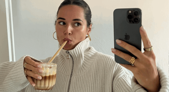 Vrouw maakt selfie met proteïne ijskoffie en telefoon, ter illustratie van zelfgemaakte Starbucks viral koffie.