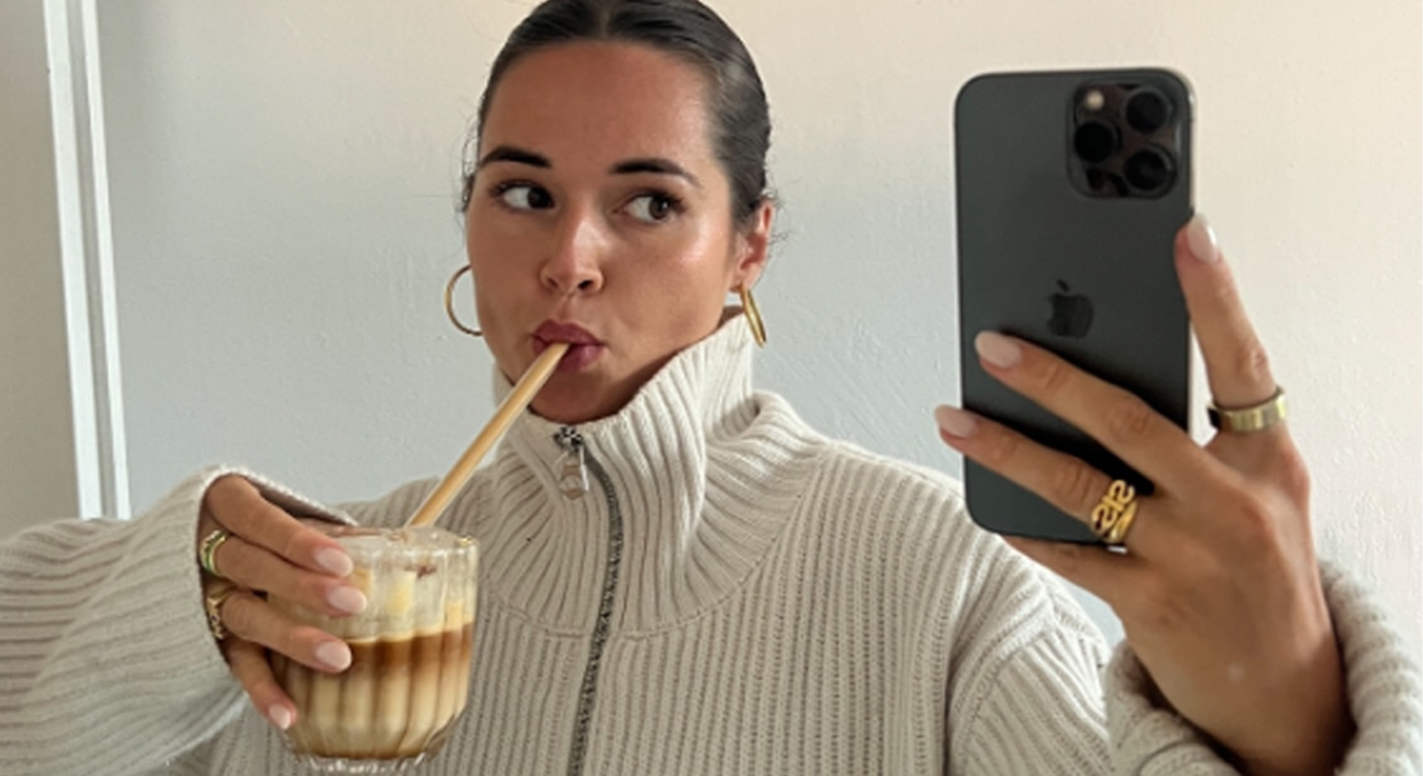 Woman takes selfie with protein iced coffee and phone, illustrating homemade Starbucks viral coffee.