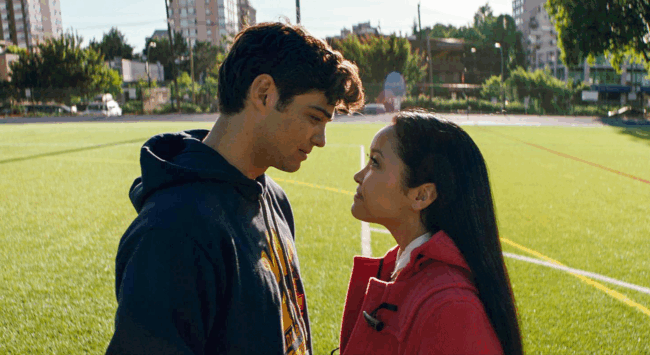 Een jong stel, een man en een vrouw, kijken elkaar intens aan op een sportveld, wat de jonge liefde, kwetsbaarheid en directe connectie van klassieke romcoms illustreert, in contrast met modern datinggedrag.