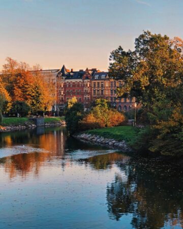 Rivier, kanaal, klassieke-gebouwen, baksteenarchitectuur, herfstbladeren, bomen, zonsondergang, gouden-uur, stadsgezicht, reflectie-water.