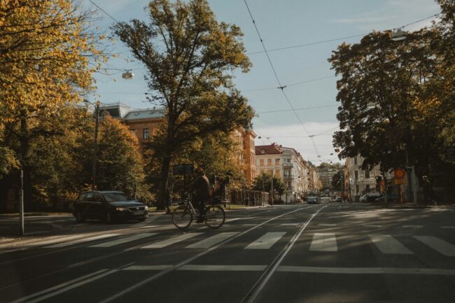 Stadsstraat, fietser, tramrails, zebrapad, herfstbomen, klassieke-gebouwen, stadsverkeer, stedelijke-omgeving, auto.