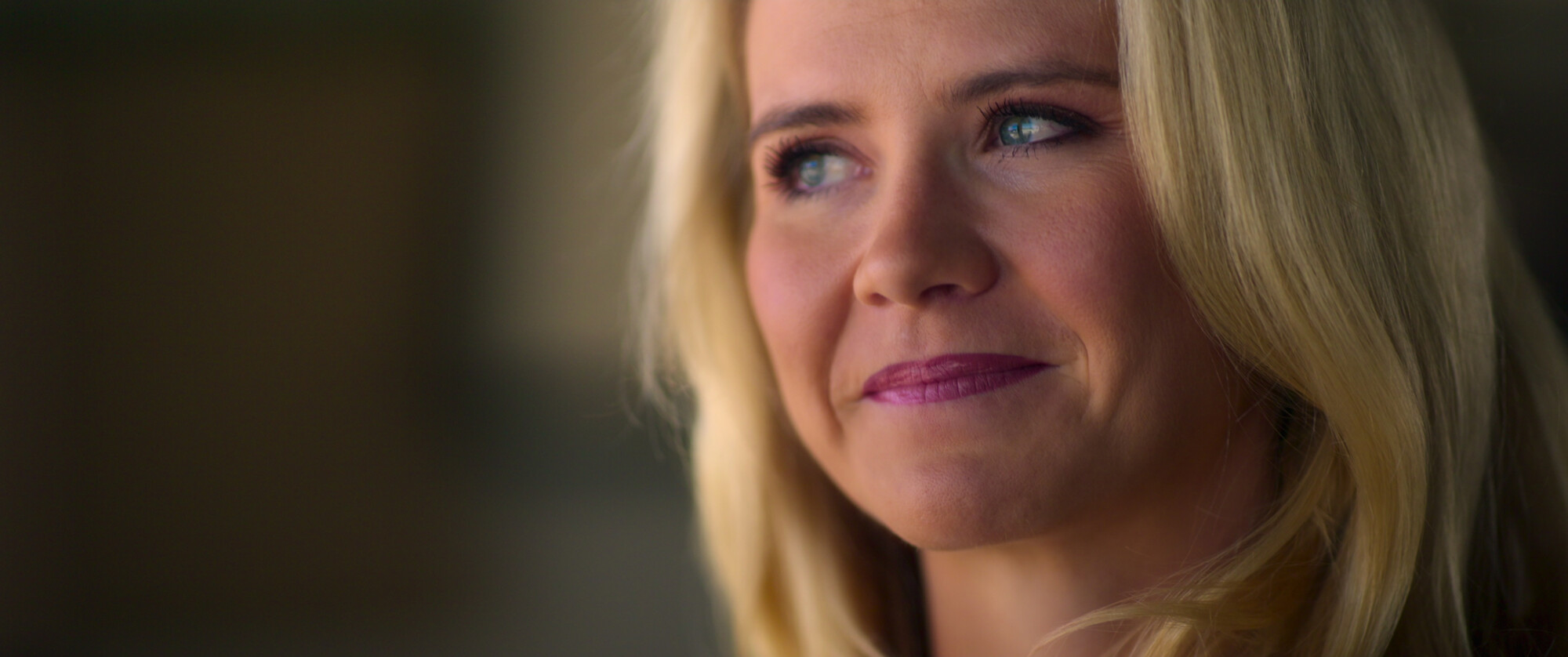"Close-up portret van een glimlachende blonde vrouw met een zachte blik en een warme lichtinval."