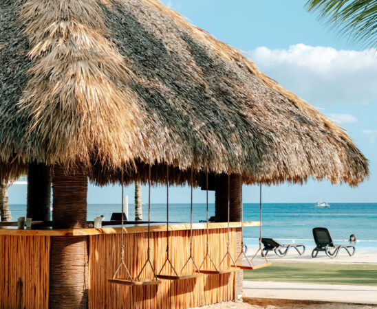 beach bar, thatched roof, wooden stools, swings, sea view, tropical resort, sunbeds, blue sky, holiday destination