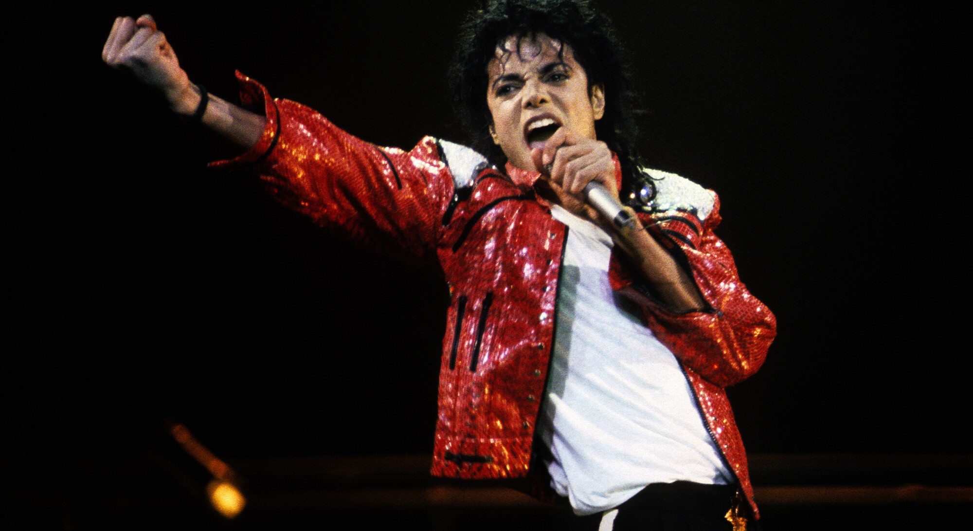 Michael Jackson during a performance, dressed in his iconic red glitter jacket and holding a microphone.