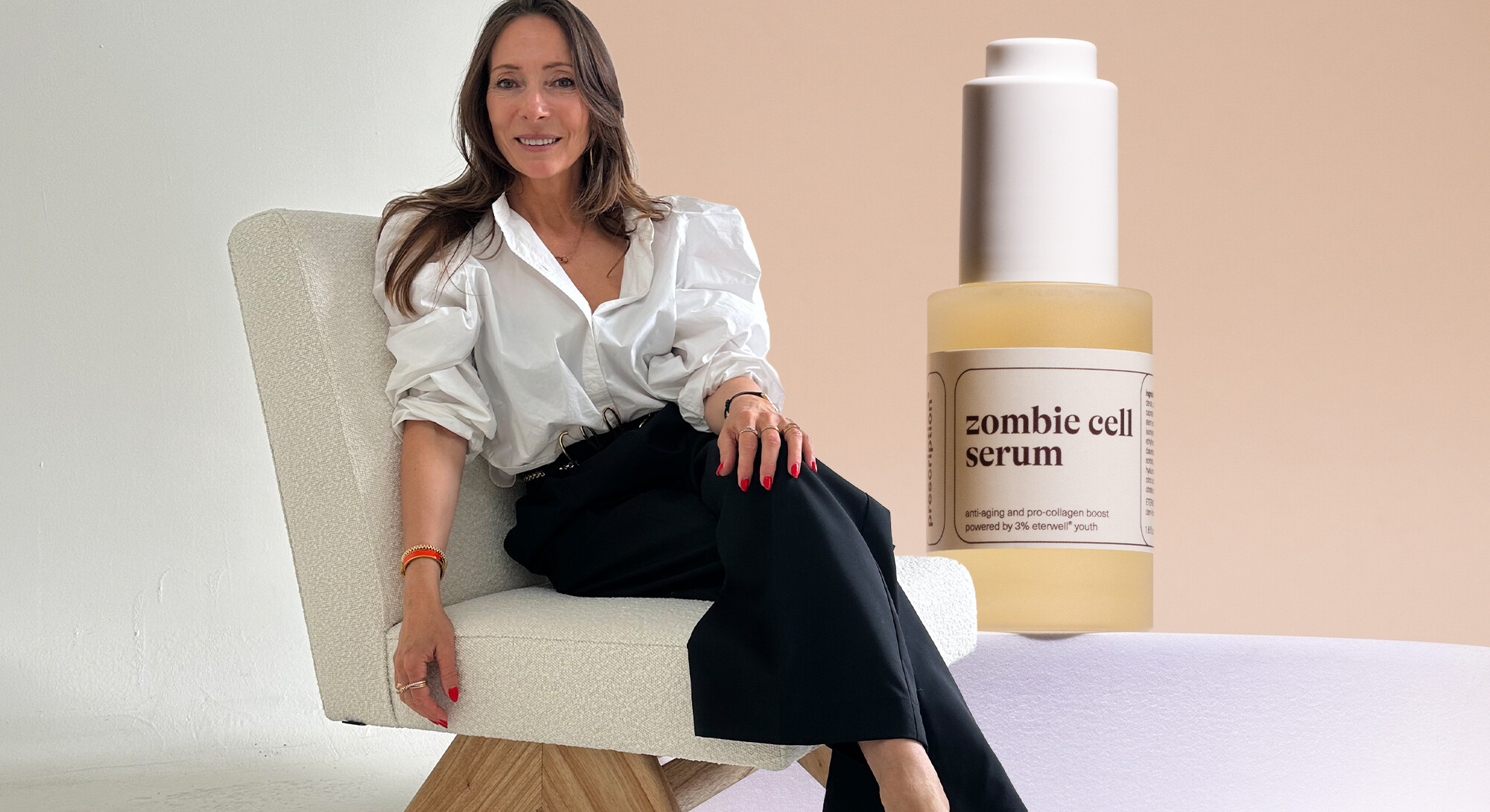 Een glimlachende vrouw in een witte blouse en zwarte broek zit op een moderne stoel, geflankeerd door een grote afbeelding van een flesje 'zombie cell serum' van Prescription.
