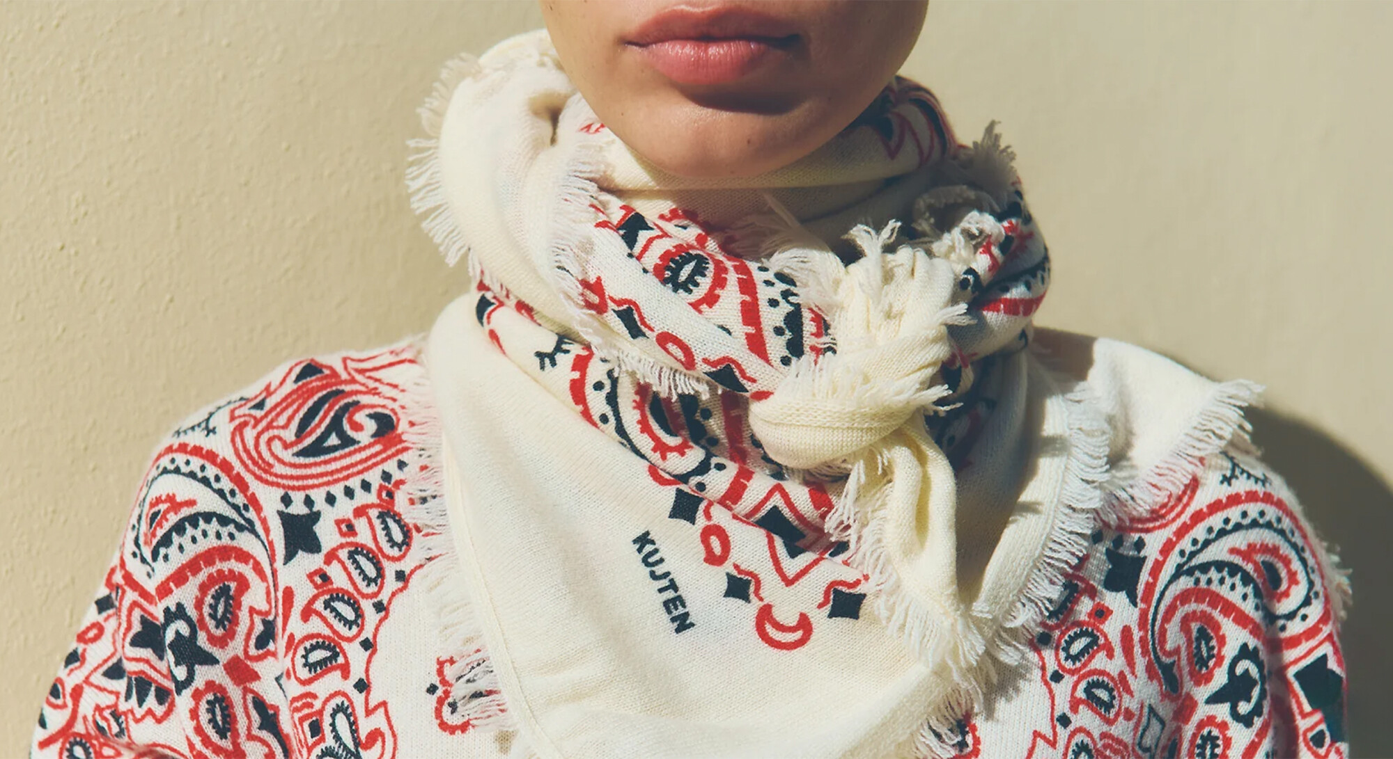 Close-up of a cream-colored cashmere bandana with a red-blue paisley pattern, tied around the neck.