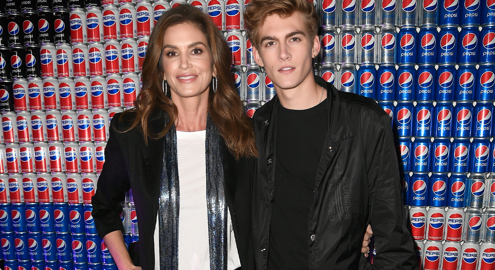 Cindy Crawford poseert samen met haar zoon voor een muur vol Pepsi-blikjes.