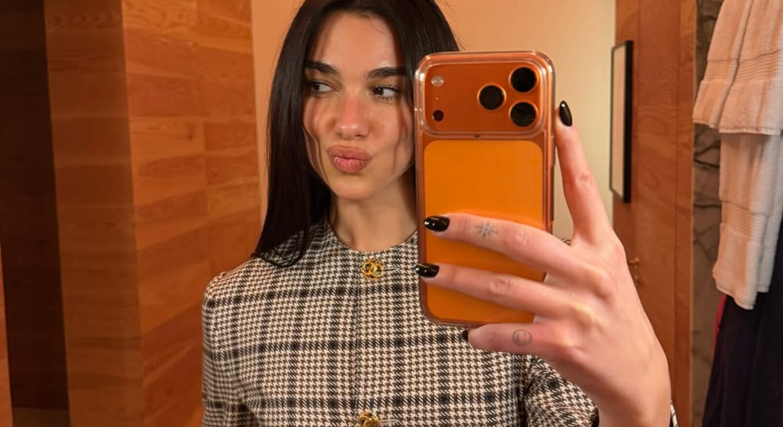 Vrouw maakt een spiegelselfie met donkerbruine nagels en een geruite jas in warme bruintinten.