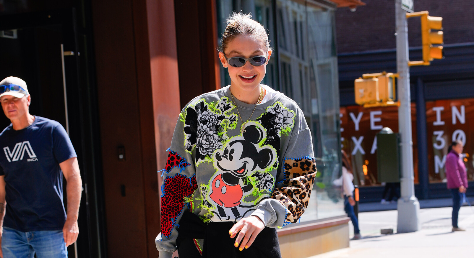 Gigi Hadid op straat lopen lachend met zonnebril en trui met Mickey mouse