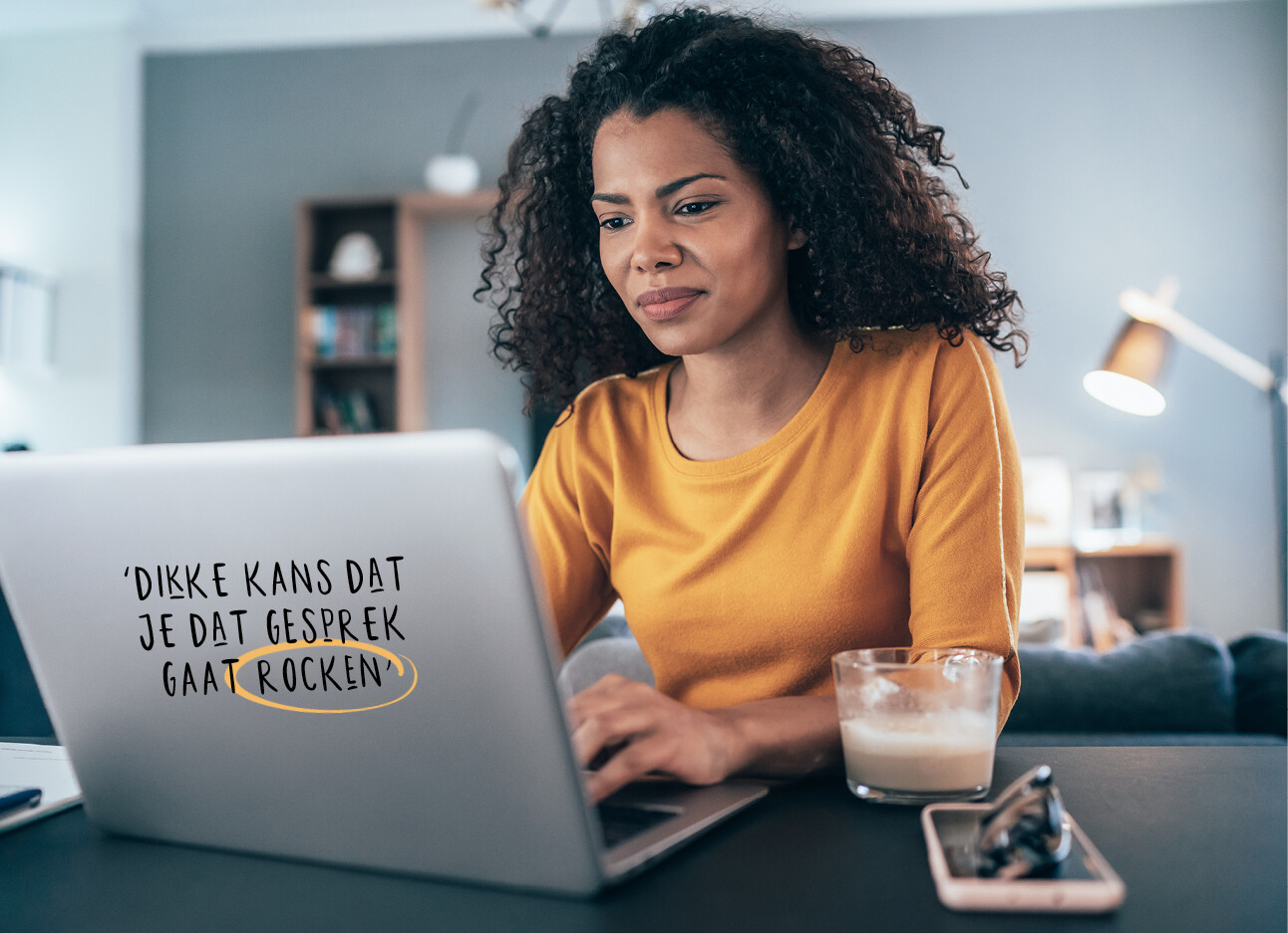 vrouw lachend achter computer met een mosterd kleurig tshirt aan het een kop koffie