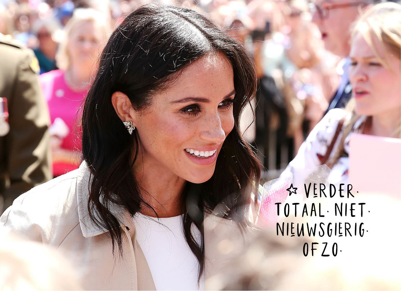 Meghan Markle lachend tussen de mensen met een wit jurkje aan en beige jas