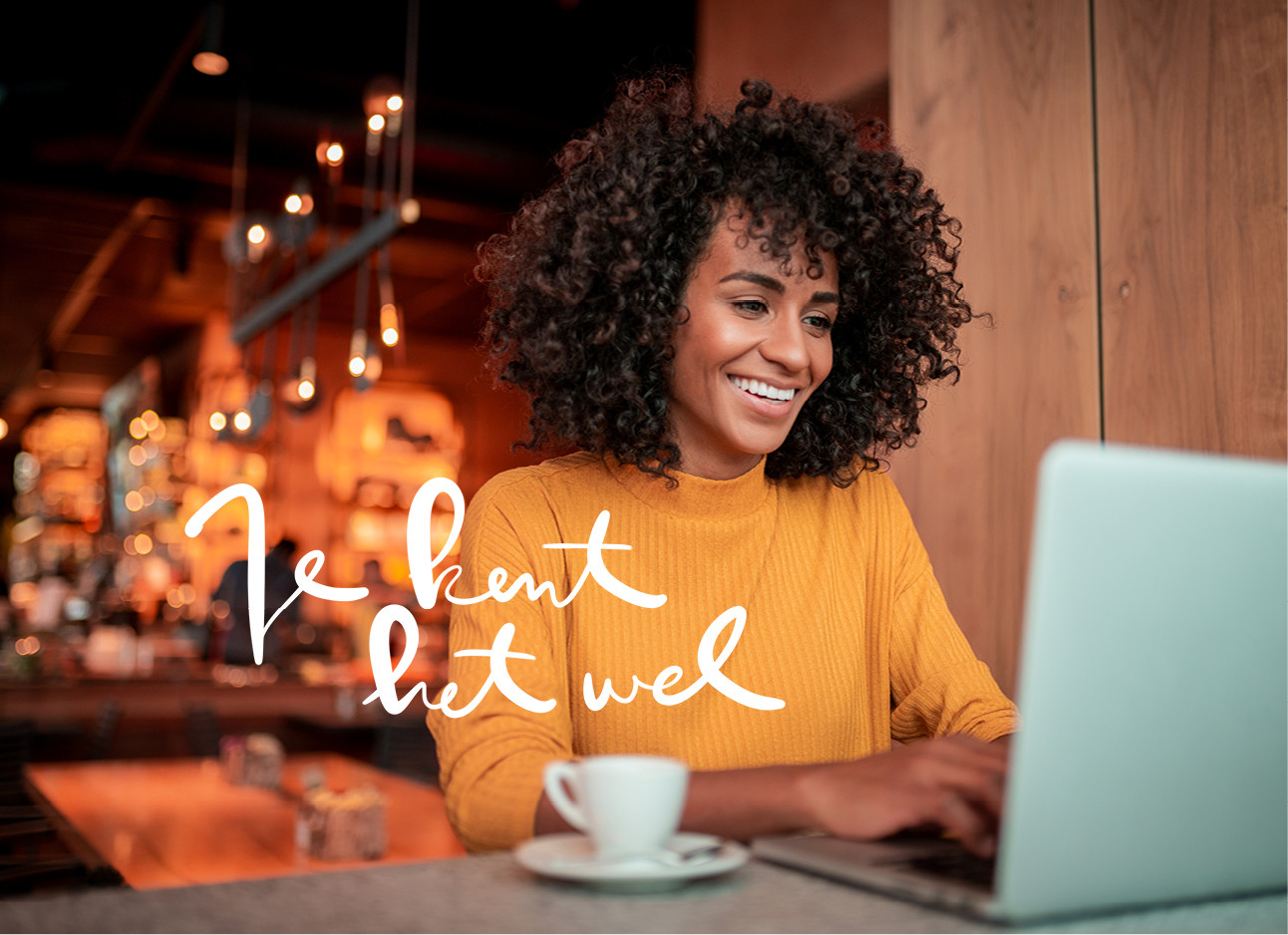 vrouw in een cafe aan het werk lachend naar haar computer tikken